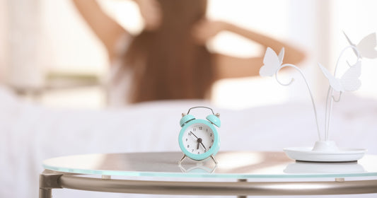 a blue alarm on the table and a lady stretching behind in the morning