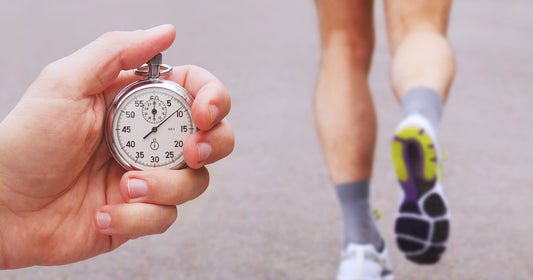 stopwatch in a hand and blurred runner athlete feet running on a road